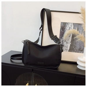 Détail d'un sac bandoulière noir minimaliste avec large sangle sur un meuble chic