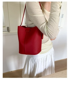 Close-up of a minimalist red bucket bag in litchi-grain leather on shoulder of a model
