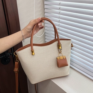 Detail of beige woven tote bag with brown leather handles and a mini bag charm