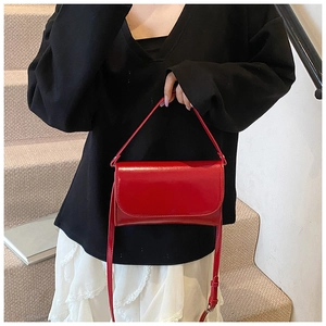 Detailoverzicht van de felrode vierkante leren handtas met schouderband op een model