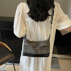 Detail of grey tweed tote bag with black leather base worn by model in white dress