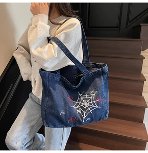 Detail of blue denim tote bag featuring white spider web and red spider embroidery