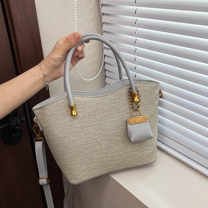 Detailed shot of a woven tote bag with grey leather handles and gold metal accents