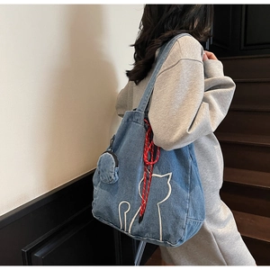Detail of blue denim tote bag featuring white cat embroidery and a red drawstring accent