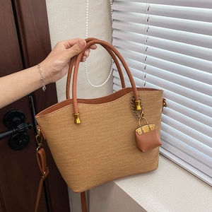 Close-up of woven straw tote bag featuring brown leather trim and metal hardware details