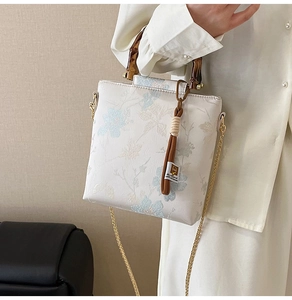 Close-up of floral crossbody bag with bamboo handle, gold chain and tassel detail