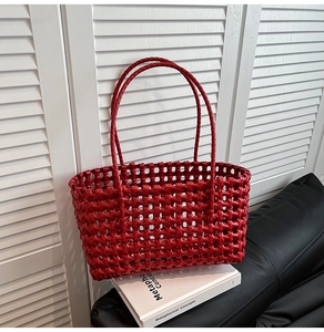 Detail view of the red woven tote bag mesh texture and slim handles on a book