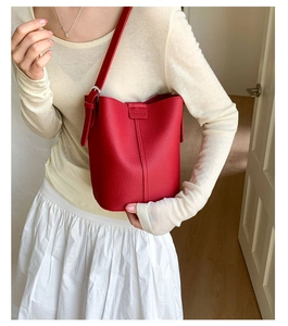 Detail of red lychee grain leather bucket bag featuring adjustable silver metal buckle strap