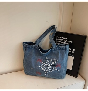 Detail of blue denim tote bag featuring white spider web and red spider embroidery motifs