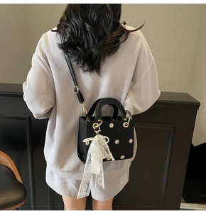 Detail of black bag with daisy embroidery, lace bow pendant, and crossbody strap display