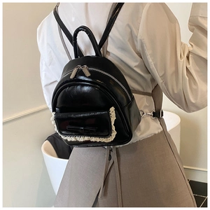 Nahaufnahme des schwarzen glänzenden Mini-Rucksacks mit weißem Spitzenbesatz und Schleife
