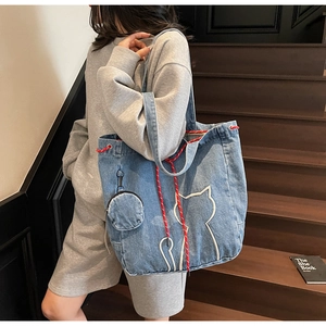 Detail of blue denim tote bag with white cat embroidery and round coin purse attachment