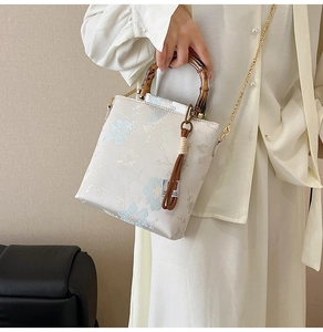Detailed embroidery on white brocade bag with bamboo handle and golden chain strap
