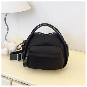 Detail of black nylon crossbody bag featuring double handles and silver metal zipper