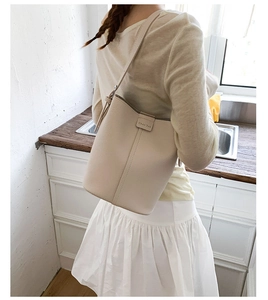 Detailed shot of beige textured leather bucket bag with a slim strap and metal logo
