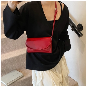 Detail van een felrode laklederen crossbodytas met een glanzende afwerking en klepsluiting