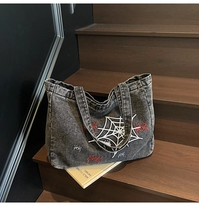 Detail of gray denim tote bag with red and white spider web embroidery on wood