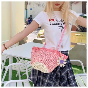 Detailed close-up of pink straw woven crossbody bag with cute white flower charm accessory