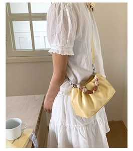 Detail of yellow pleated cloud bucket bag with marble bead handle and shoulder strap