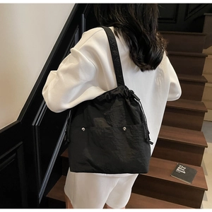 Detail of black drawstring nylon tote bag featuring silver rivets and industrial pleats