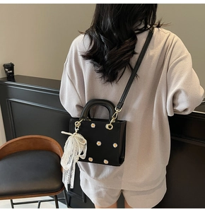 Detail of black daisy print handbag featuring a pearl and lace charm with gold hardware