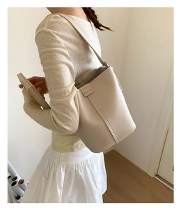 Close-up of beige lychee grain leather bucket bag with elegant stitched details and logo