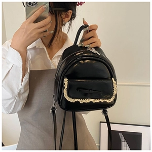 Detail eines schwarzen Mini-Rucksacks mit cremefarbener Spitze und kleiner Schleife