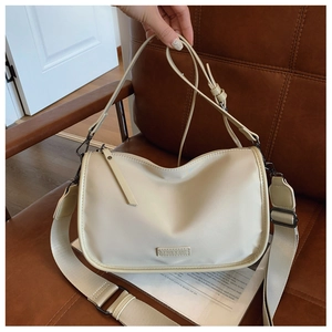 Détail du sac bandoulière beige minimaliste avec large sangle sur une chaise en cuir vintage