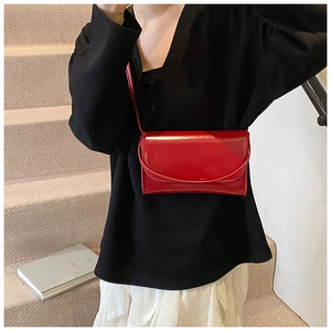 Detail van een glanzende rode rechthoekige laklederen crossbody tas met overslag