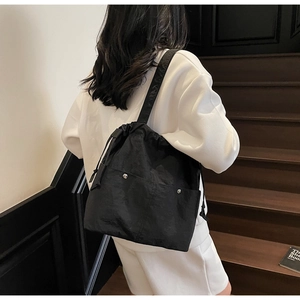 Detailed view of black nylon drawstring bucket bag with metal snap pockets on model