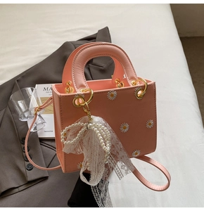 Detail of pink crossbody bag with daisy embroidery, gold ring handle, and pearl lace charm