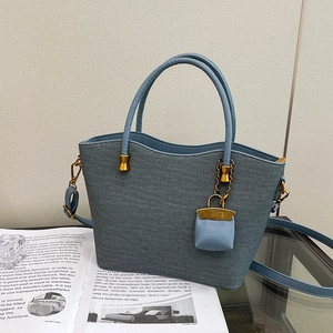 Detail of light blue woven tote bag with scalloped edge and golden mini charm attachment