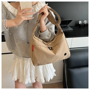 Detail view of khaki nylon tote bag with red tag and black logo in casual office setting