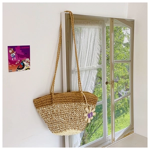 Detail of woven straw tote bag with floral charm and bicolor pattern on white wall