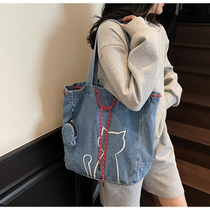 Close-up of blue denim tote bag featuring white cat embroidery and woven drawstring detail