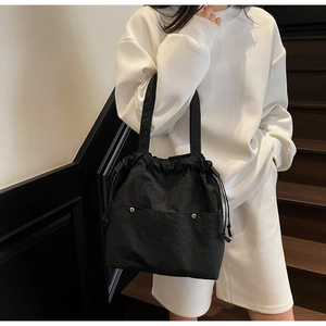 Detail of black nylon tote bag featuring drawstring closure and front pocket with silver buckle