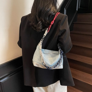 Detail of light blue denim tote with red and blue rope knot strap and silver chain accent