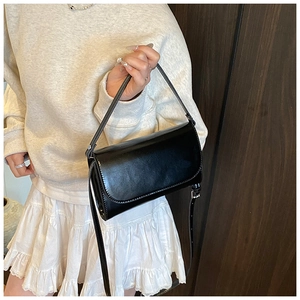 Detail van glanzende zwarte mini-tas met strakke klepsluiting en dunne schouderbandjes