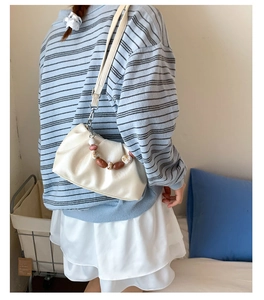 Detailed view of cream dumpling bag with ruched texture and marble bead handle strap