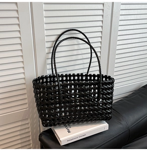 Close-up of black woven tote bag texture and handles placed on a white book and leather sofa
