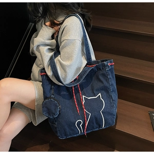 Detail of blue denim tote bag with cat embroidery and a small round coin purse accessory