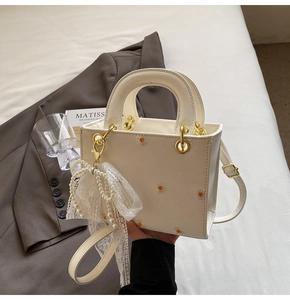 Detail of cream white handbag with daisy embroidery, pearl bow charm and gold handle