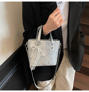 Nahaufnahme einer silbernen Mini-Beuteltasche mit Schlangenmuster und weißer Schleife