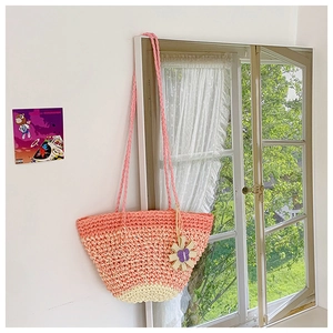 Detail of woven straw tote bag with pink gradient finish and floral butterfly charm