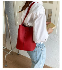 Detail of red bucket bag in litchi grain leather worn over a white shirt