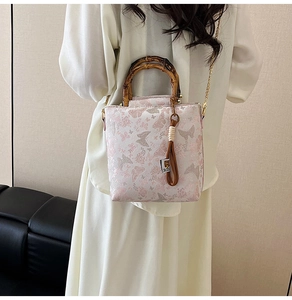 Detail of white butterfly lace bag featuring a natural bamboo handle and gold chain strap
