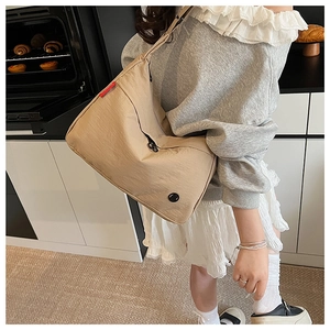 Detail of khaki nylon crossbody bag with wide strap and side red tag in warm kitchen setting