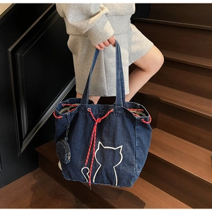 Detail of a large denim tote bag featuring white cat embroidery and a small coin purse