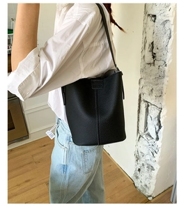 Detail of a black lychee texture leather bucket bag with a slim shoulder strap on a model
