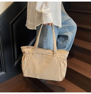 Détail d'un grand sac cabas beige avec plis latéraux et rivets tenu par un mannequin